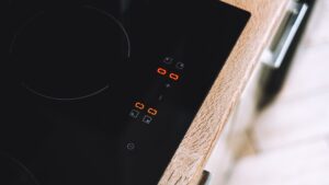 A black glass cooktop with orange segment displays lit on the touch control strip beside a wooden counter edge