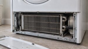 The open base panel of a laundry dryer showing a block of closely packed aluminum cooling fins