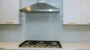 A stainless chimney range hood mounted above a gas cooktop between white wall cabinets