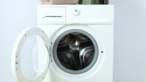 A white front load washing machine with its door open, folded towels stacked on top and a wicker basket in front